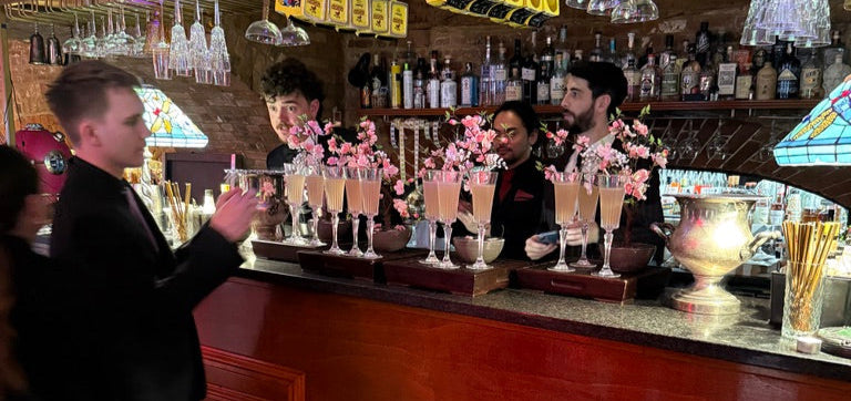 People at a bar with decorative glasses and bottles on shelves.